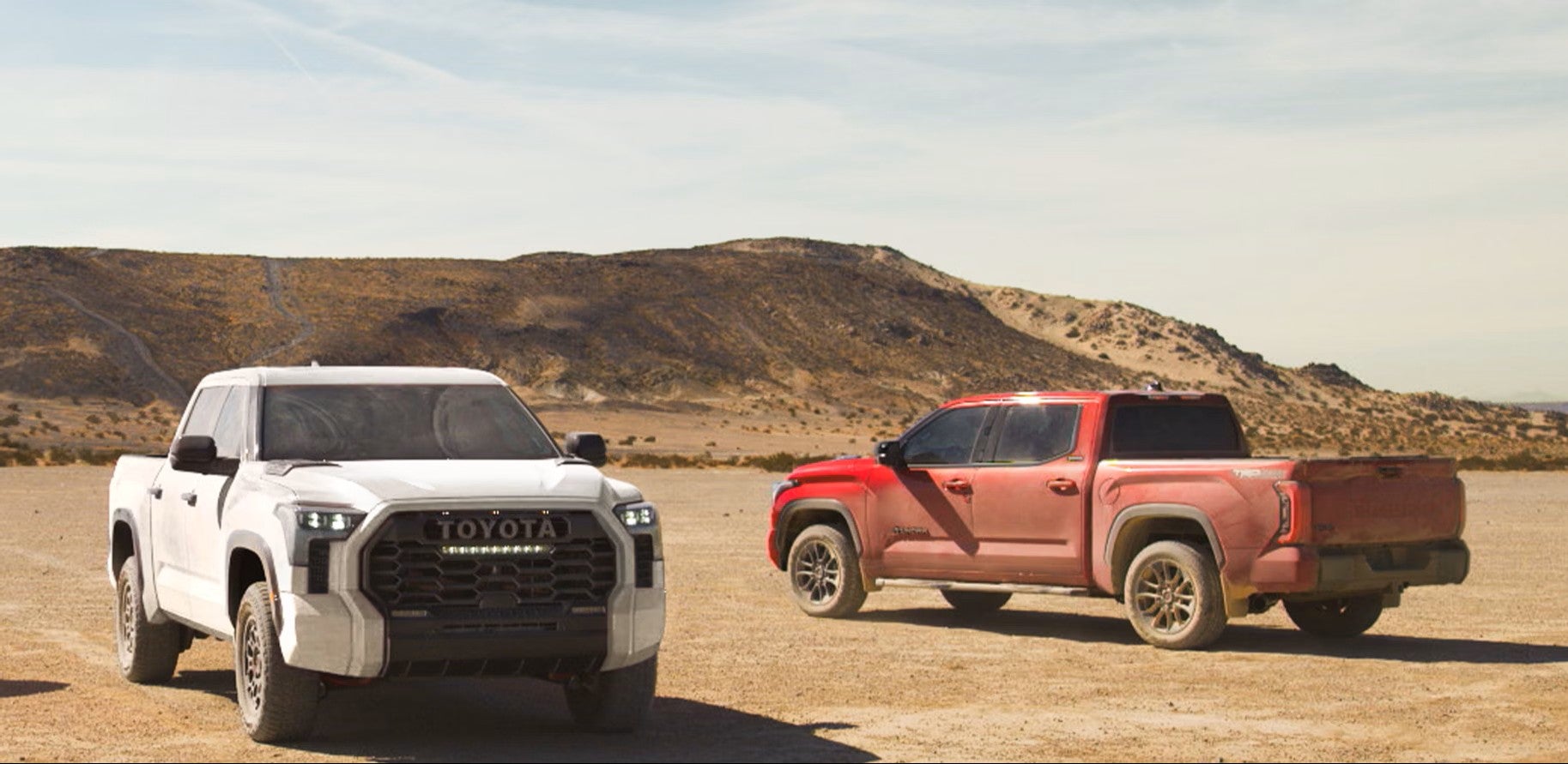 White Toyota Tundra TRD Pro with the TOYOTA grille next to a red Tundra with the TRD Off-Road package in the desert