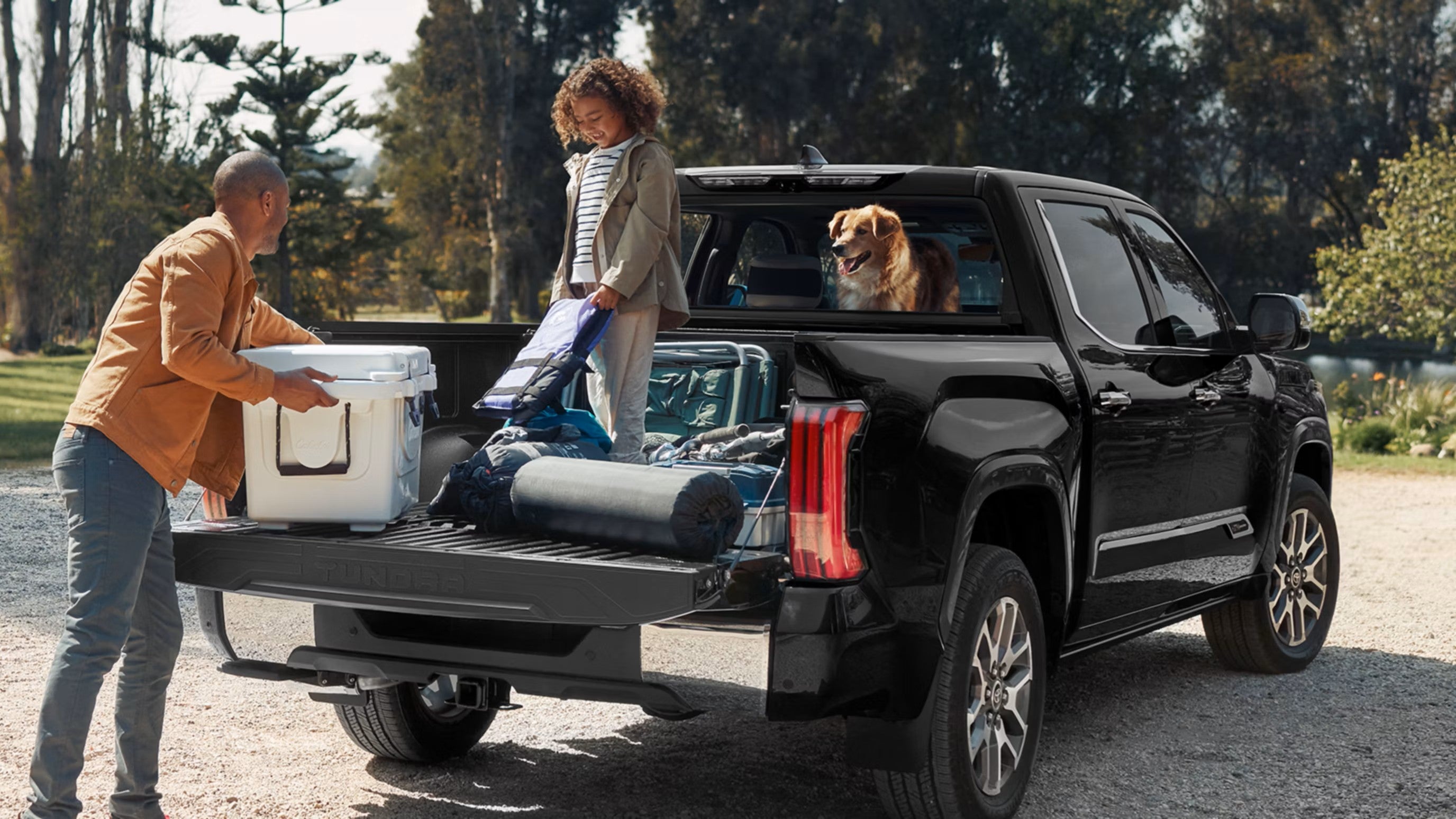 Family loading a cooler and camping gear onto the lowered tailgate of a black Toyota Tundra