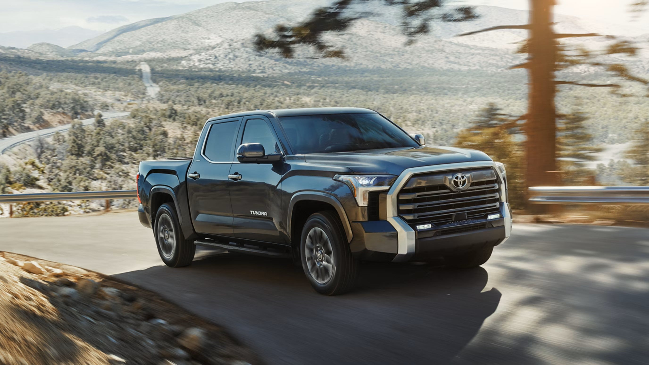 Dark gray Toyota Tundra CrewMax driving on a mountain road, front three-quarter view