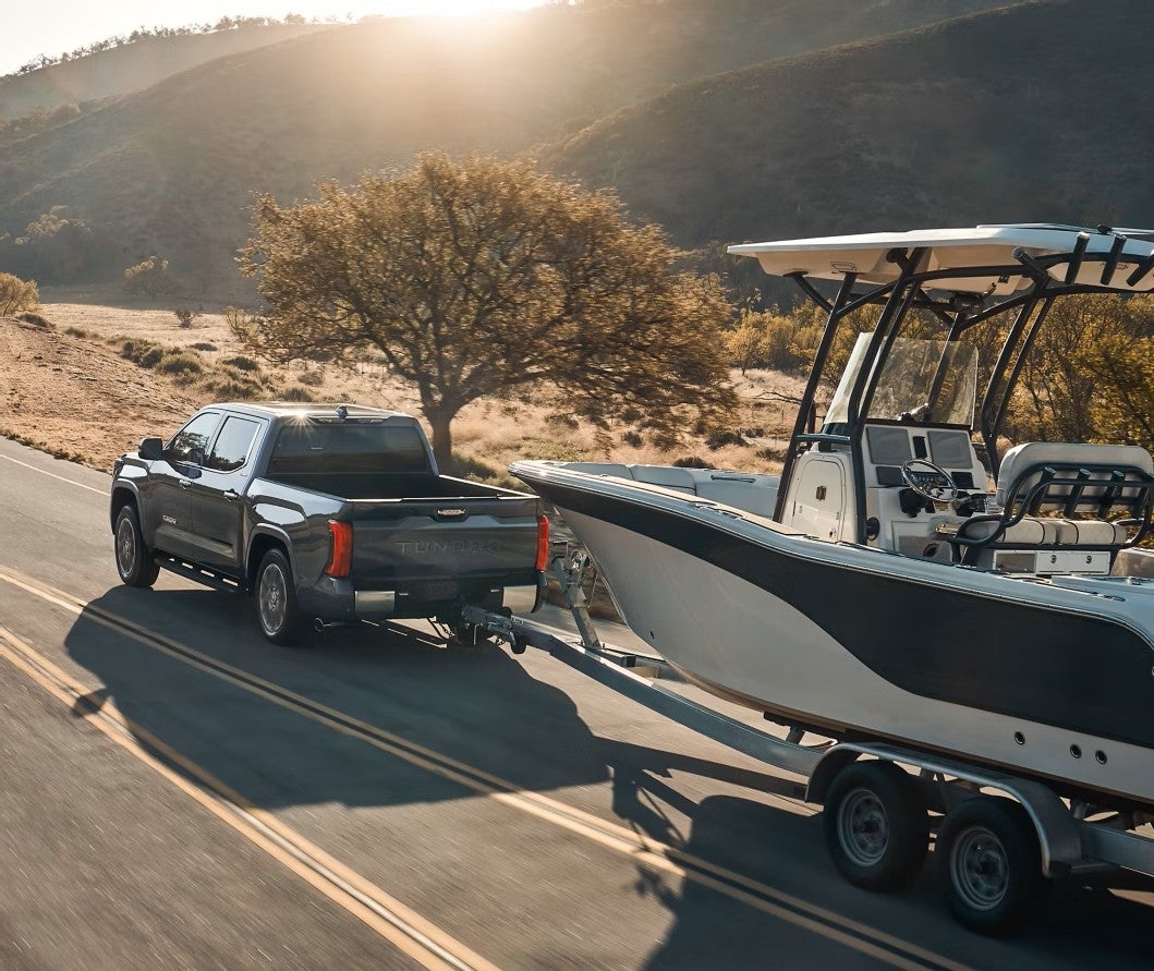 Toyota Tundra towing a boat on a trailer along a sunlit mountain road